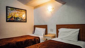 A hotel room with two single beds, a small bedside table, a wall-mounted light, and a painting on the wall.