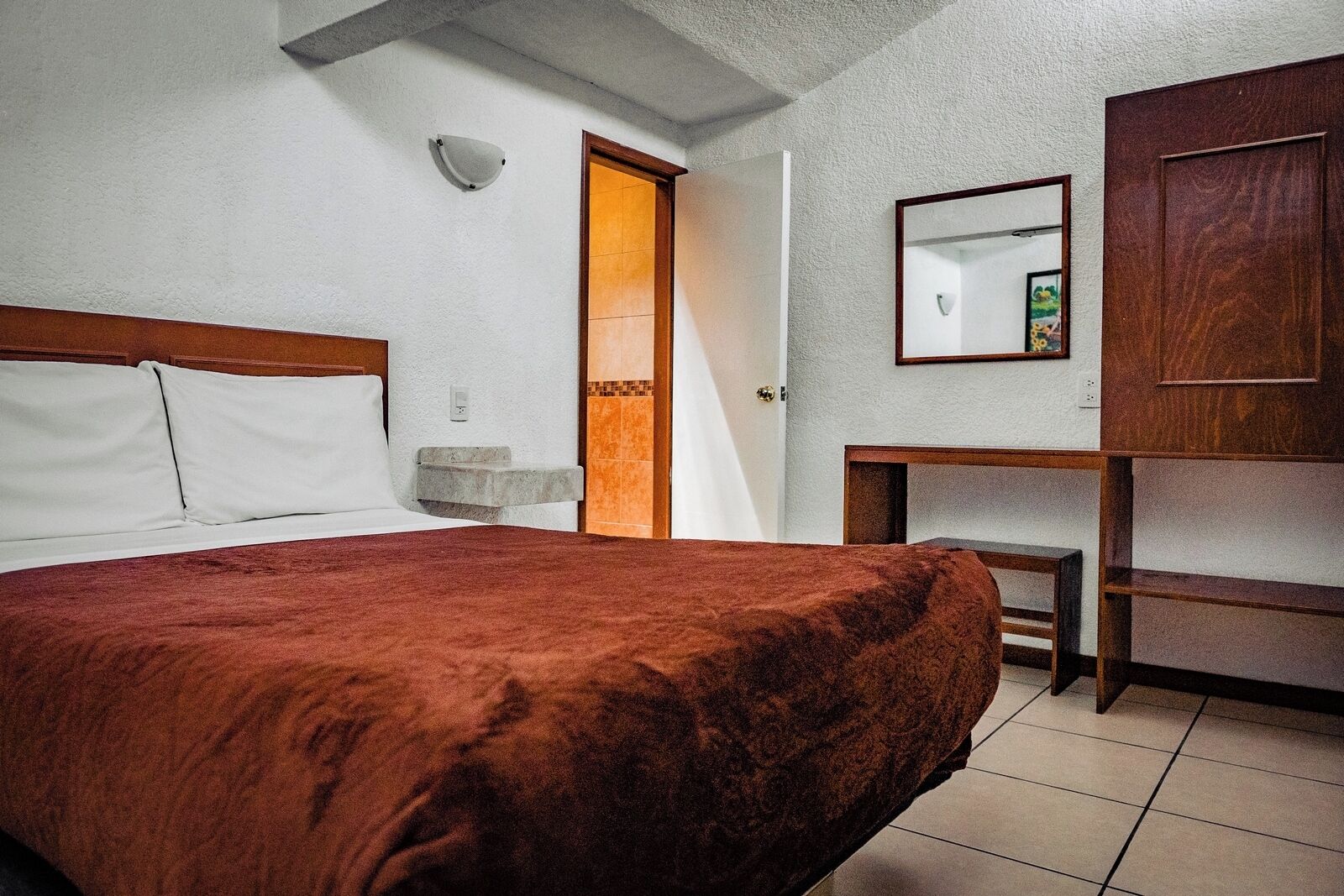 A hotel room with a bed, a bedside table, a mirror, and a wardrobe.