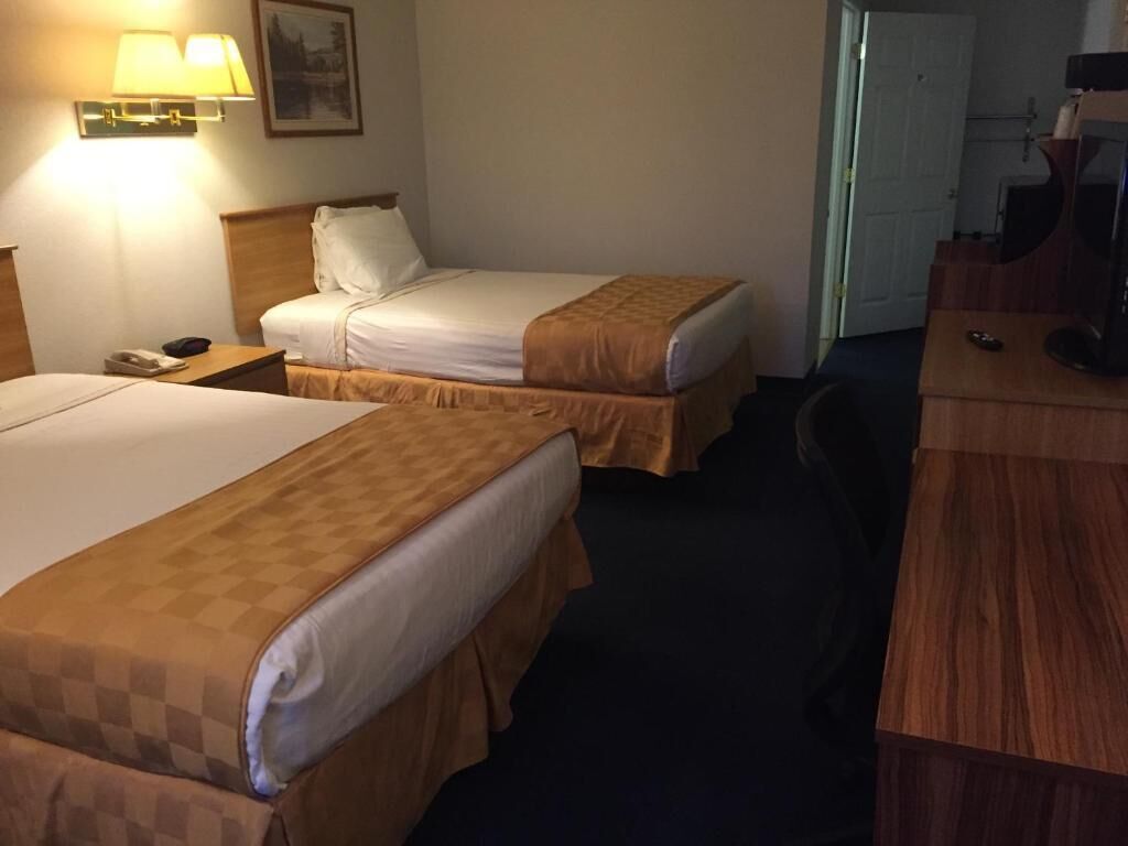 A hotel room with two beds, a desk, a chair, and a television.