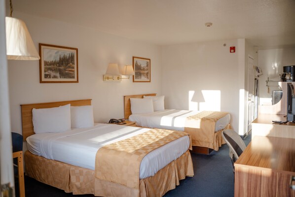 A hotel room with two beds, a desk, a chair, a television, and two wall-mounted lamps.