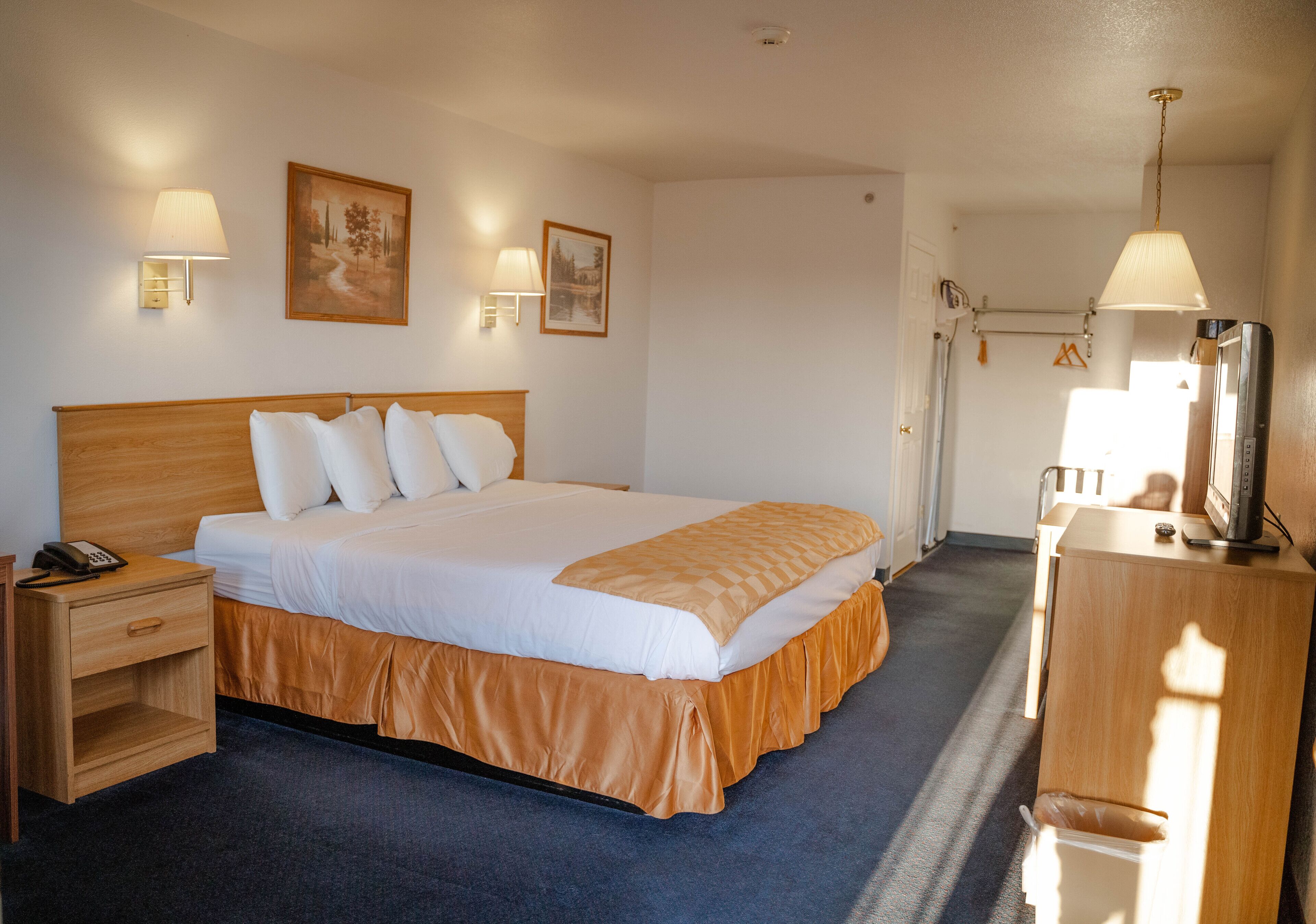 Ein Hotelzimmer mit einem großen Bett, Nachttischen, einem Schreibtisch mit Computer und Wandlampen.