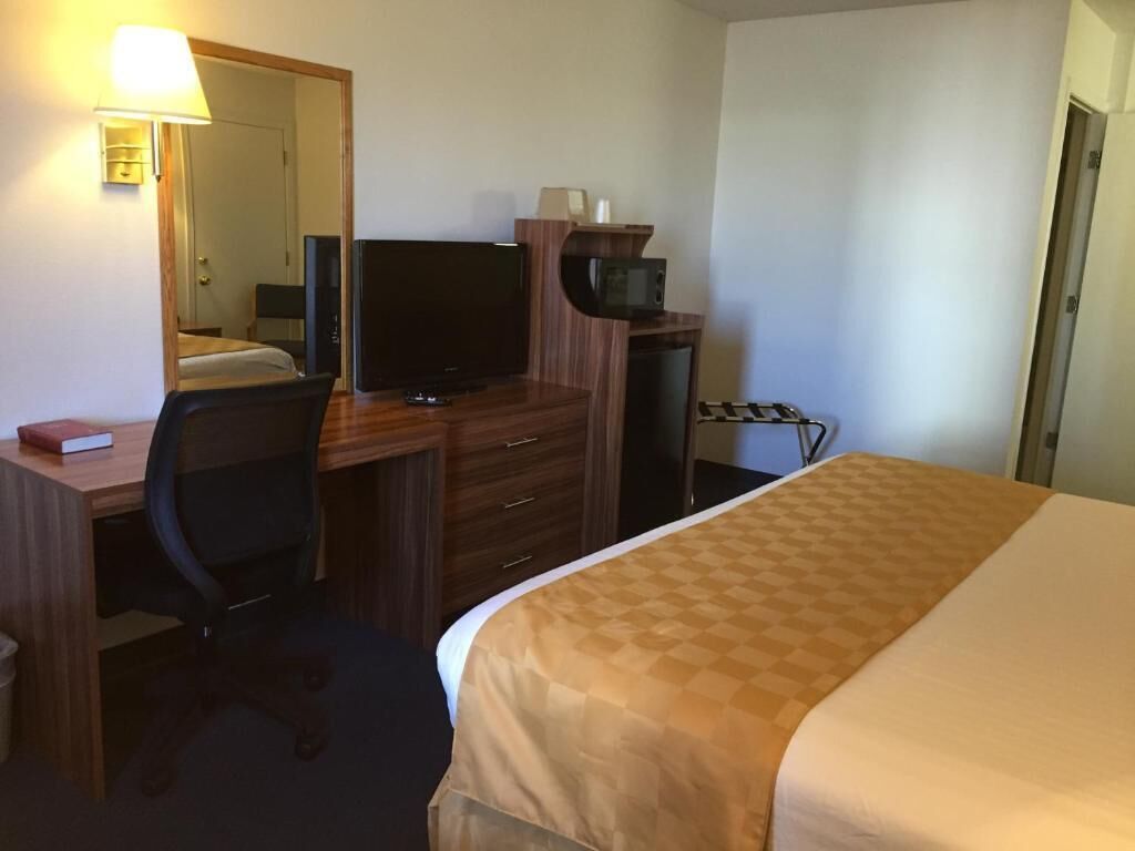 Een hotelkamer met een bed, een bureau met een computer, een stoel, een televisie en een magnetron.