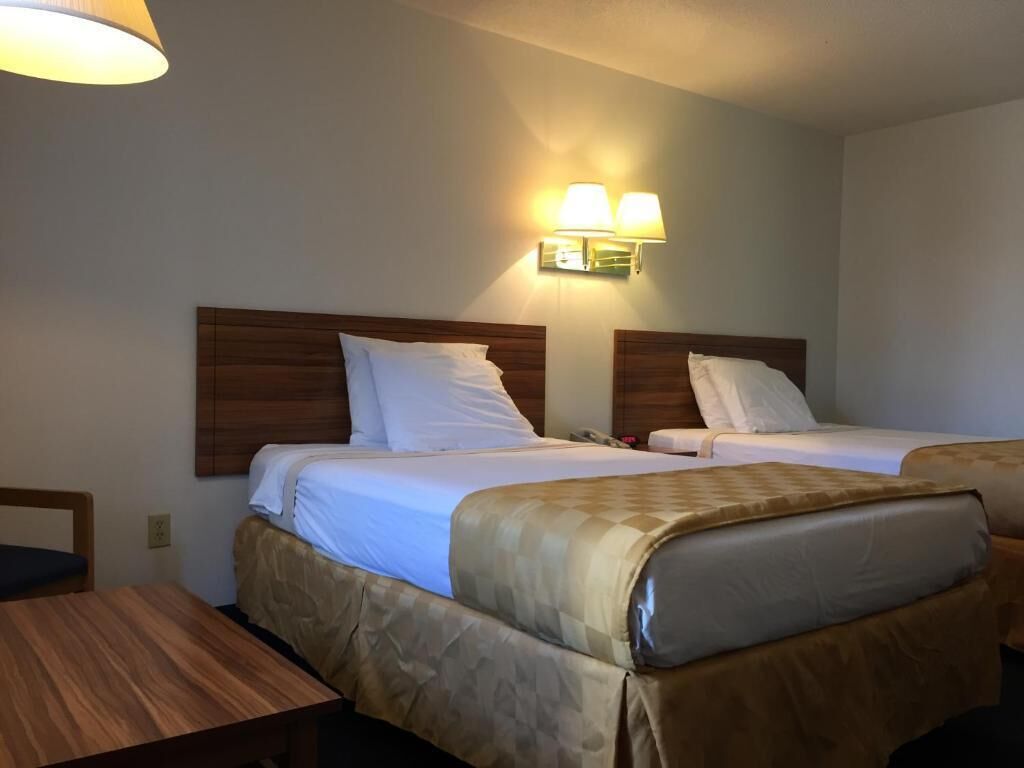 Een hotelkamer met twee bedden, een houten hoofdeinde, een tafel en een wandlamp.