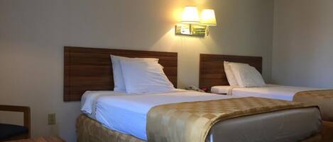 A hotel room with two beds, a wooden headboard, a table, and a wall-mounted lamp.