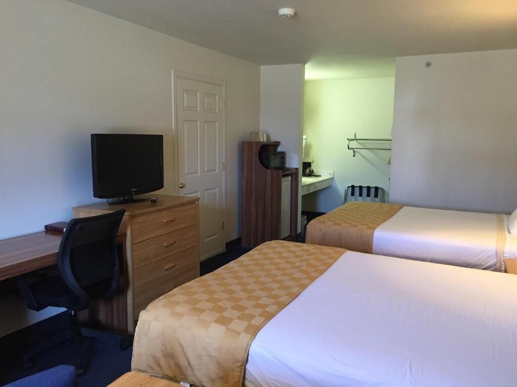 Una habitación de hotel con dos camas, un escritorio con computadora, televisor y armario.