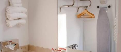 Baño con lavamanos, espejo, toallero y ropa colgada.