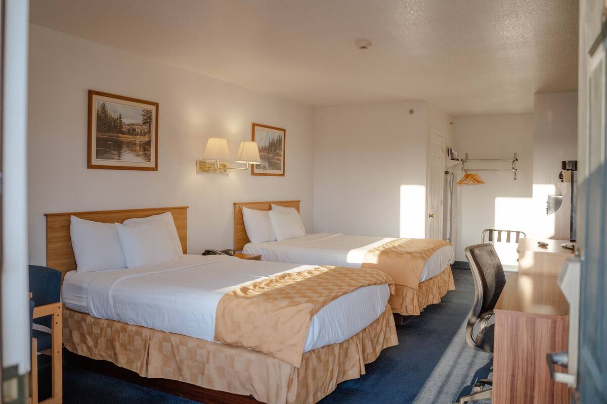 Habitación de hotel con dos camas, un escritorio, una silla y un perchero.