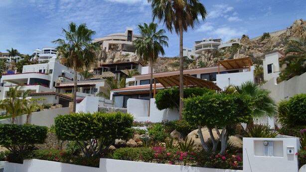 Una zona residencial en una ladera con casas blancas modernas, palmeras y un paisaje rocoso.