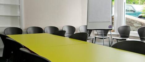 A conference room with a yellow table, black chairs, a whiteboard, and a view of a swimming pool through large windows.