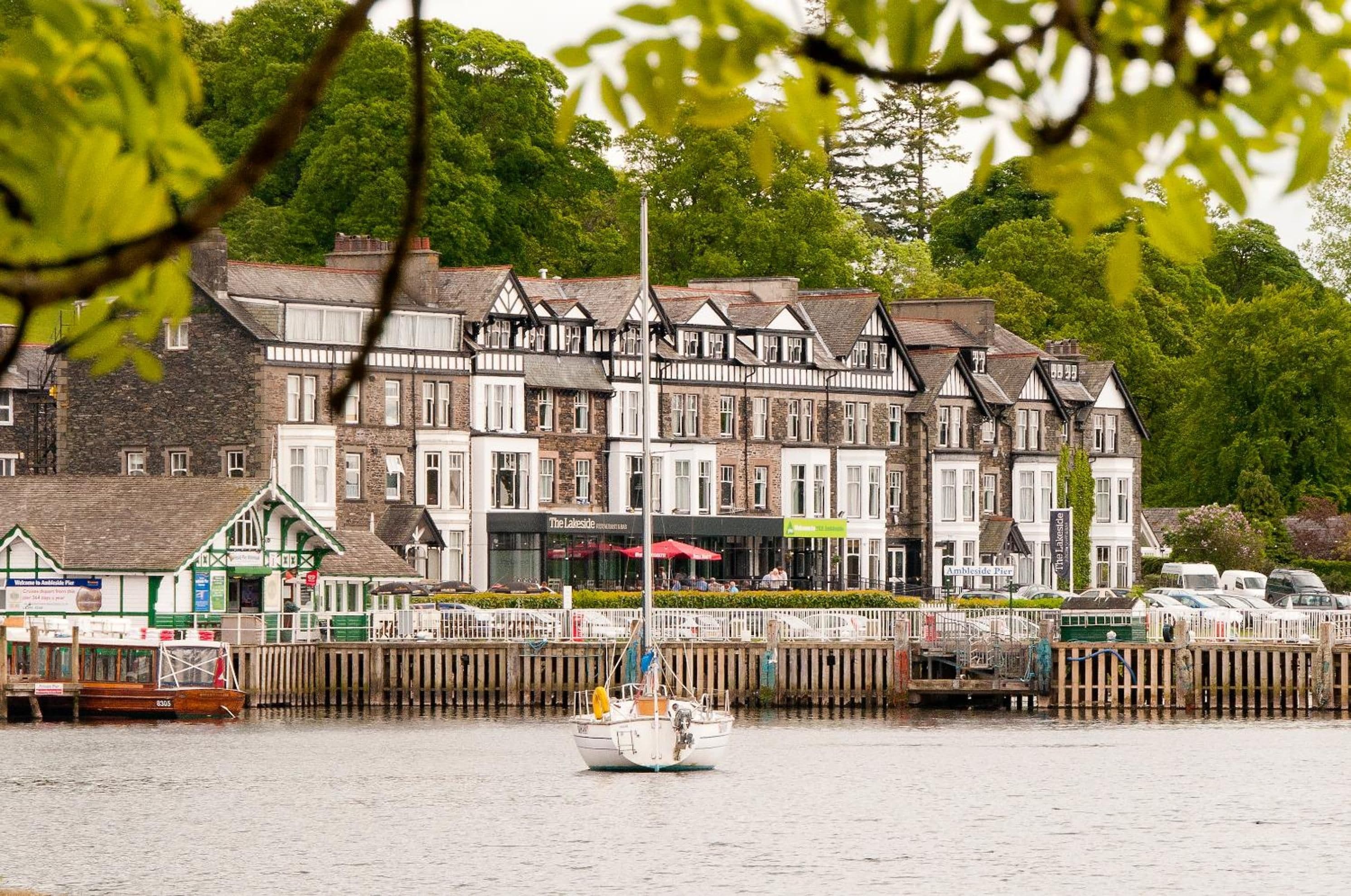 A waterfront hotel with multiple stories, a dock with a boat, and a pier with a sign.