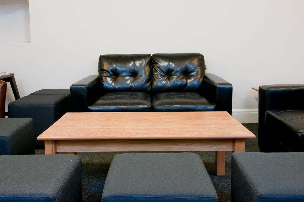 A room with a black leather sofa with tufted backrests, a wooden coffee table, and matching ottomans.