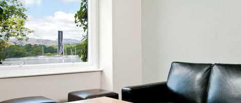 A room with a wooden table, two black leather chairs, and a window offering a view of a lake with boats and greenery.
