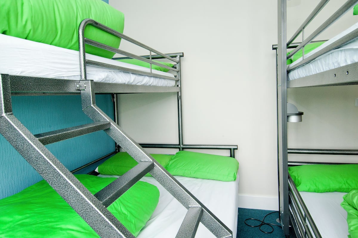A bunk bed room with green bedding and metal railings.