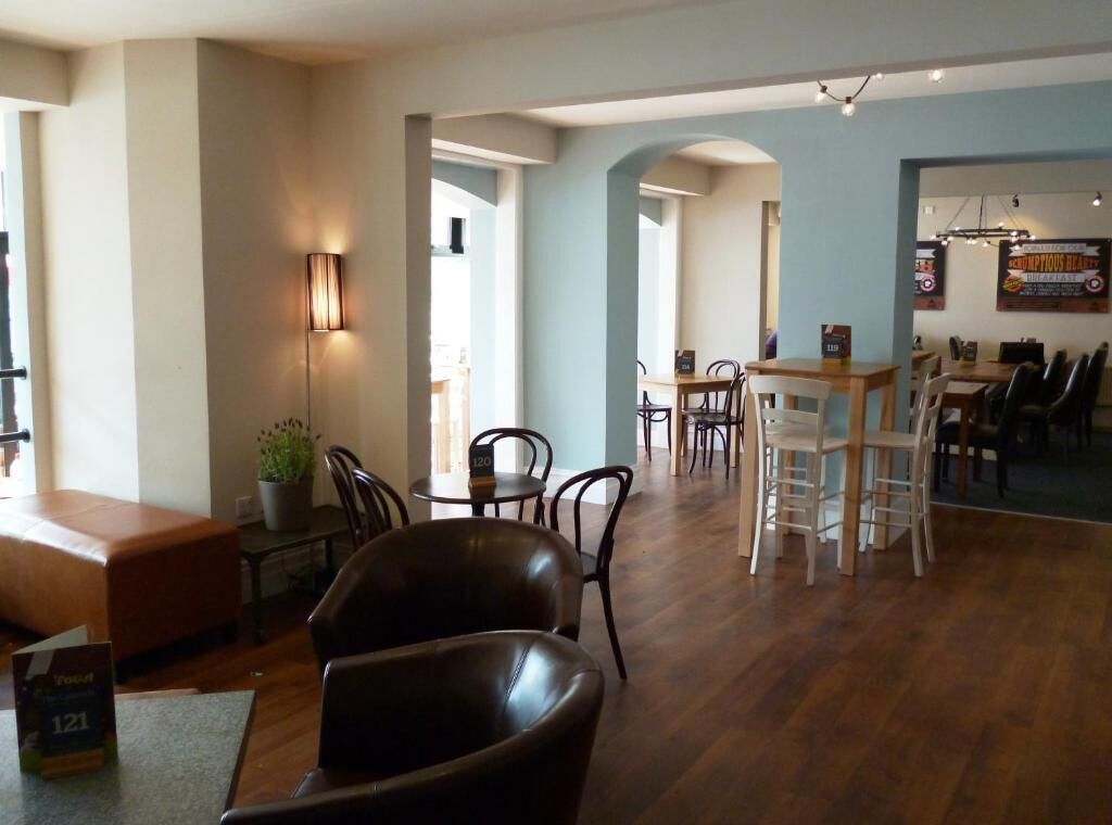 A spacious dining area with wooden tables and chairs, a bar area with stools, and a seating area with a sofa and chairs.