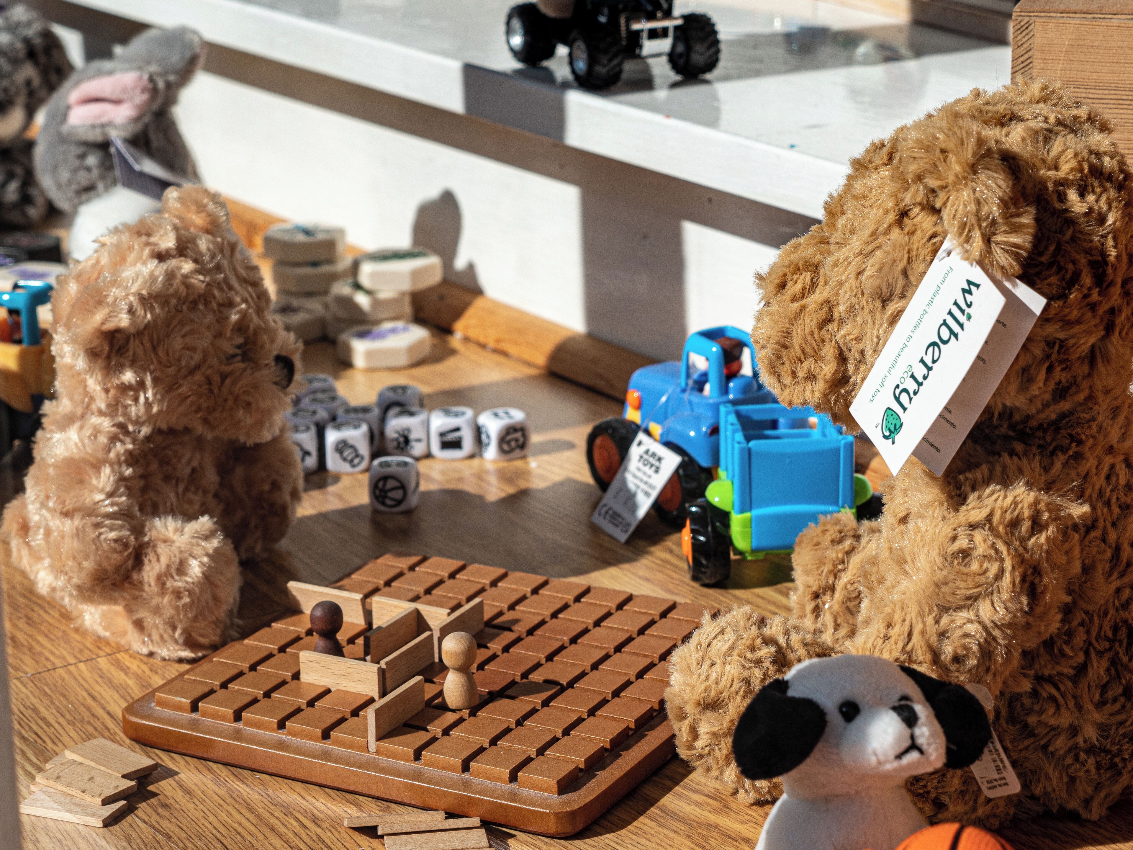 Un juego de mesa de madera con dados y fichas, un camión de juguete y dos osos de peluche sobre una mesa.