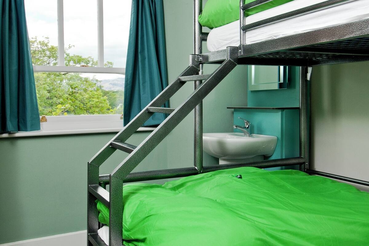 A bunk bed with a ladder, a sink, and a window with curtains.