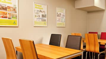 A conference room with wooden tables and chairs, posters on the wall, and a ceiling light.