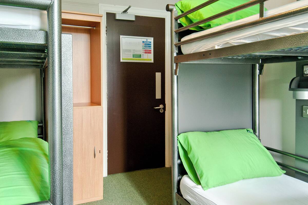 A bunk bed room with green bedding, a wooden door, and a fire action poster on the wall.