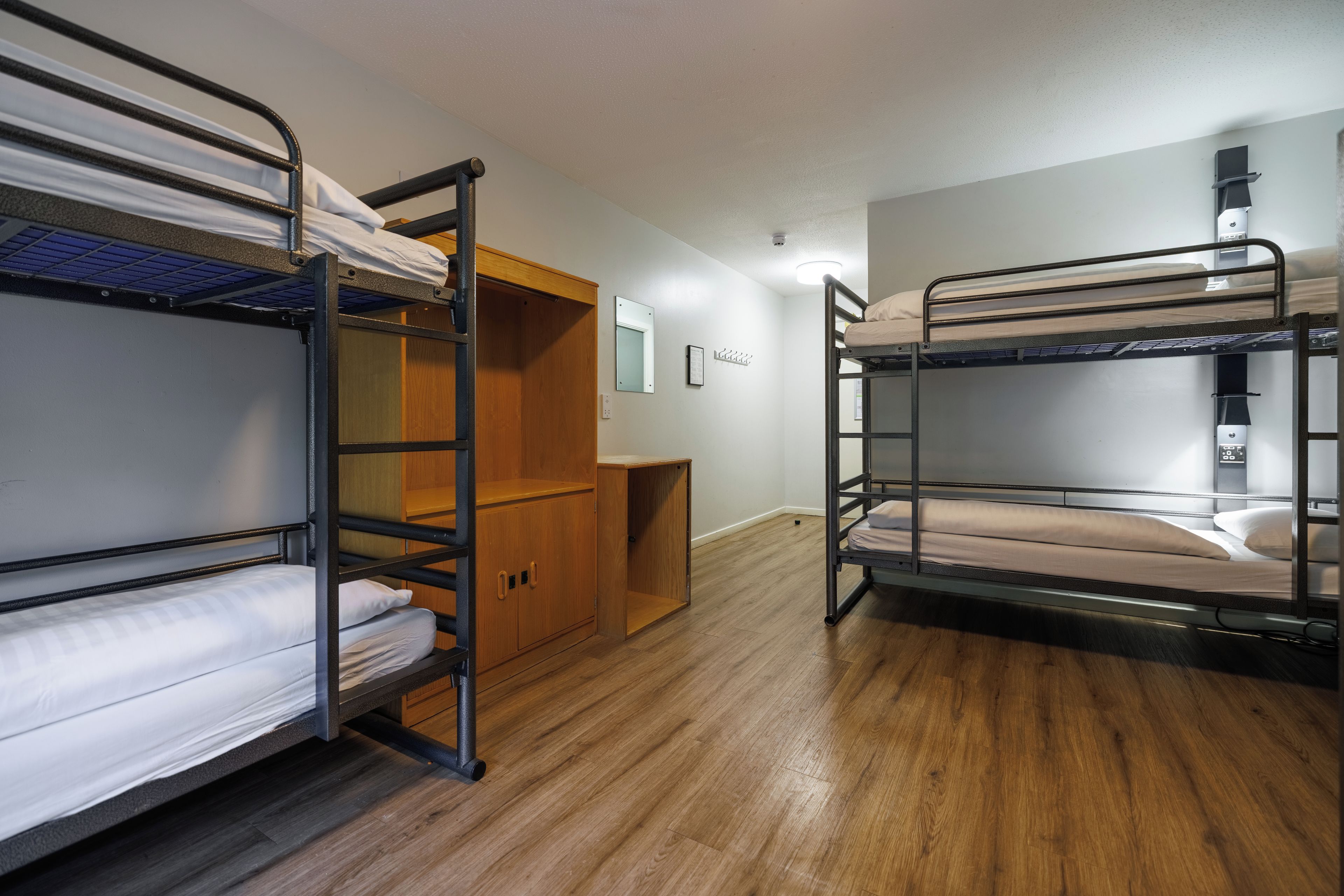 Une chambre de dortoir avec des lits superposés, une armoire en bois et un bureau.