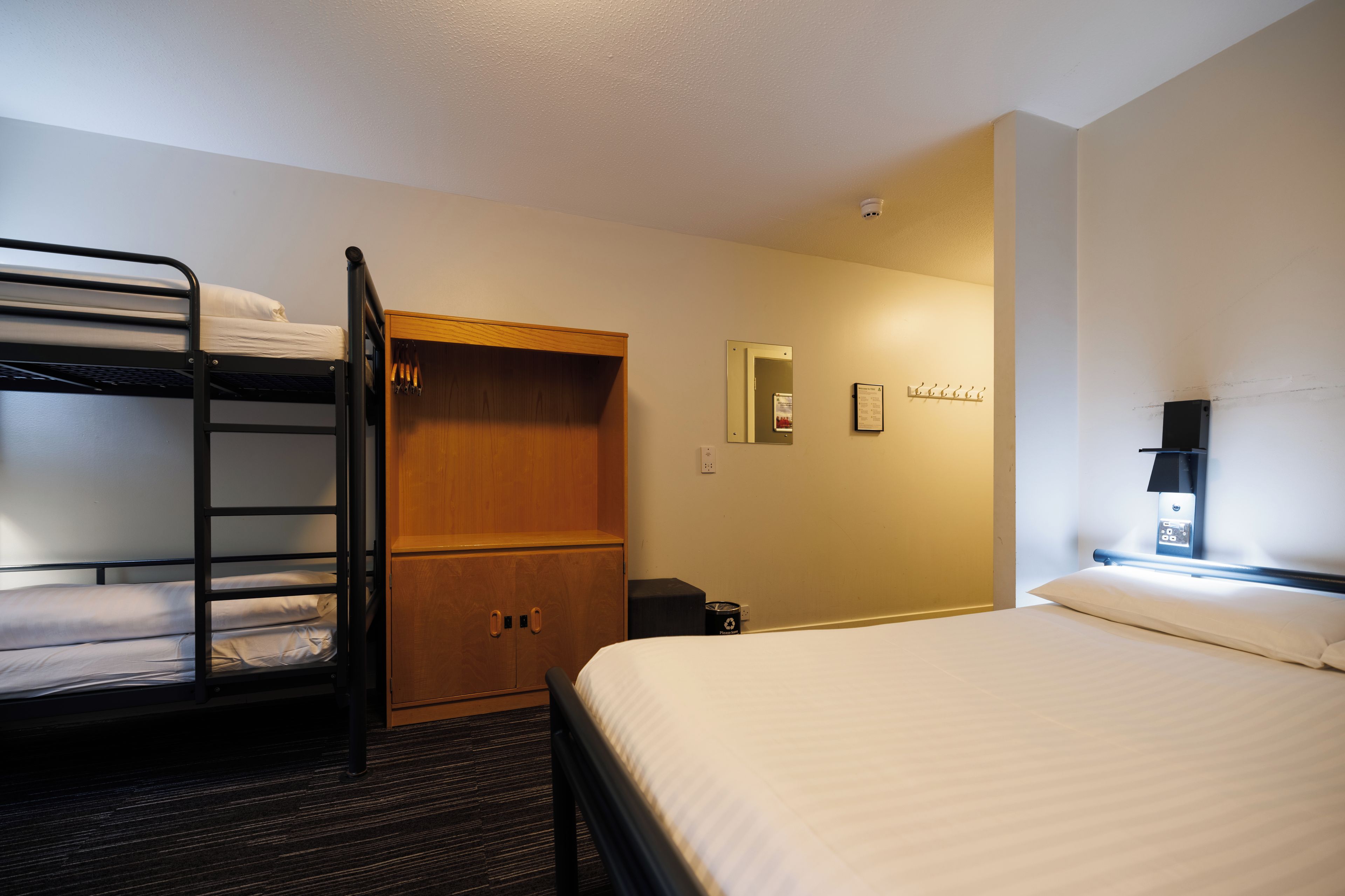 A hotel room with bunk beds, a wooden wardrobe, a mirror, a small desk, and a nightstand.