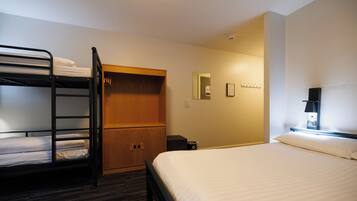A hotel room with bunk beds, a wooden wardrobe, a mirror, a small desk, and a nightstand.
