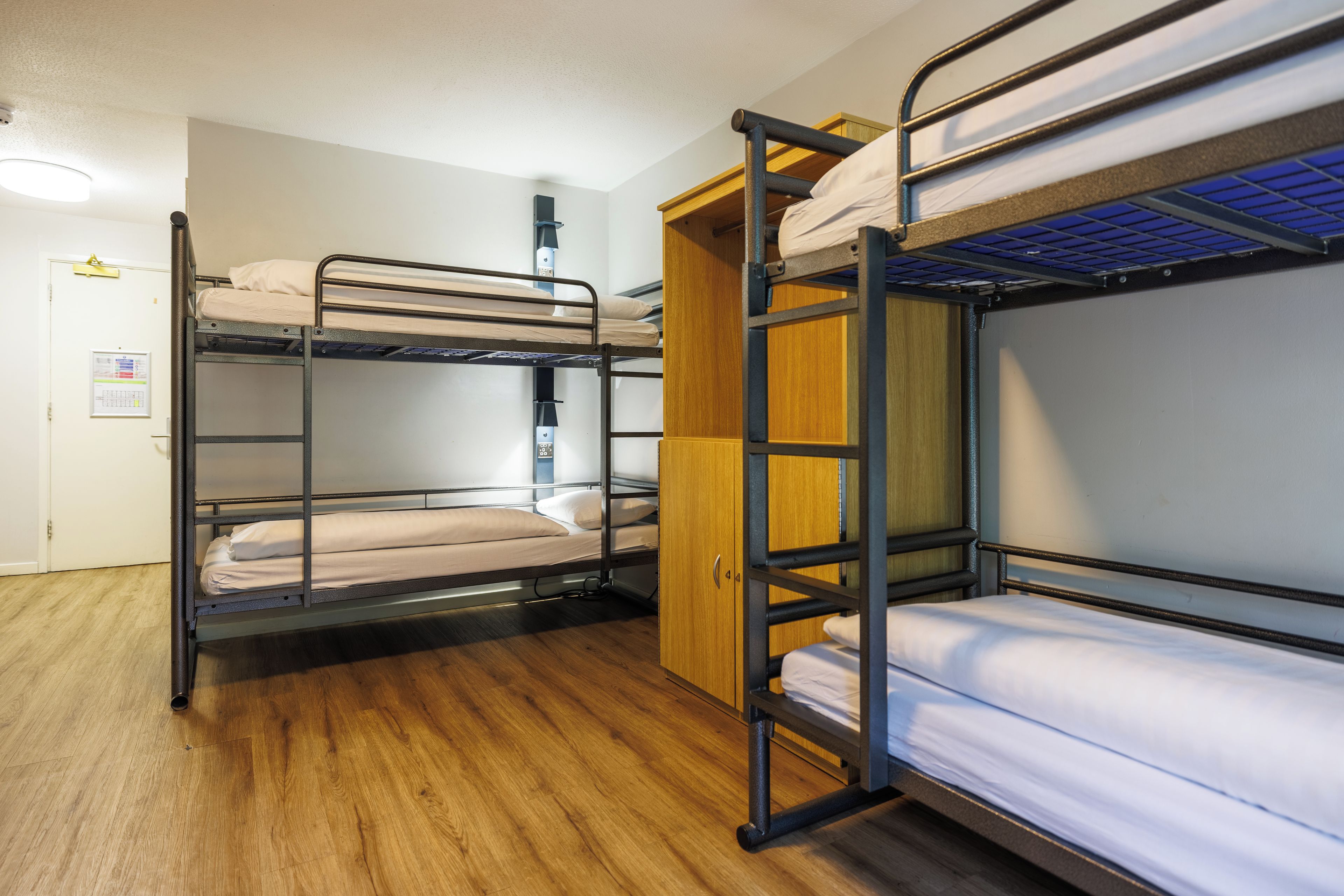 Dormitorio con literas, un armario de madera y una puerta con un aviso.