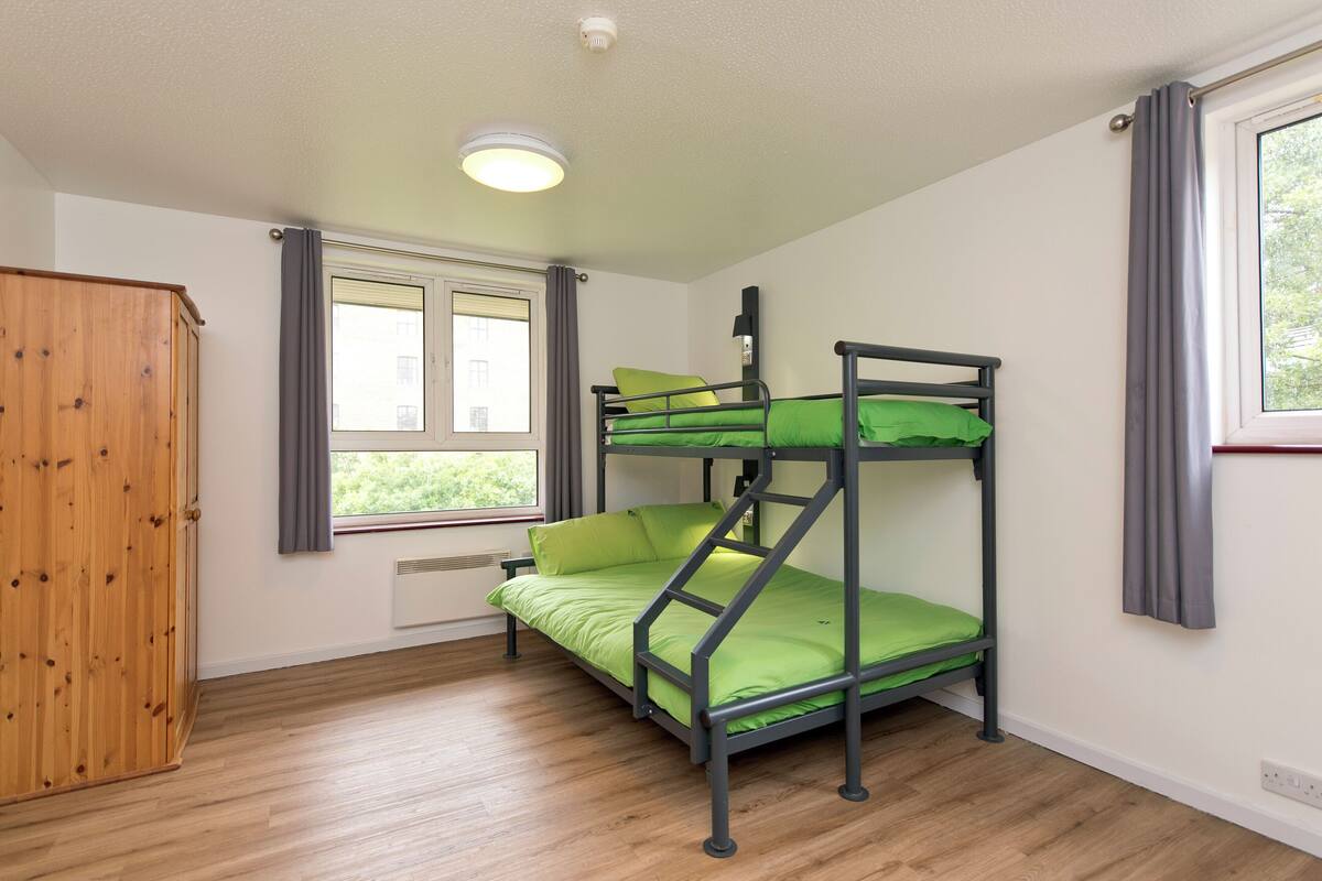 A bunk bed room with a wooden wardrobe and a window with curtains.