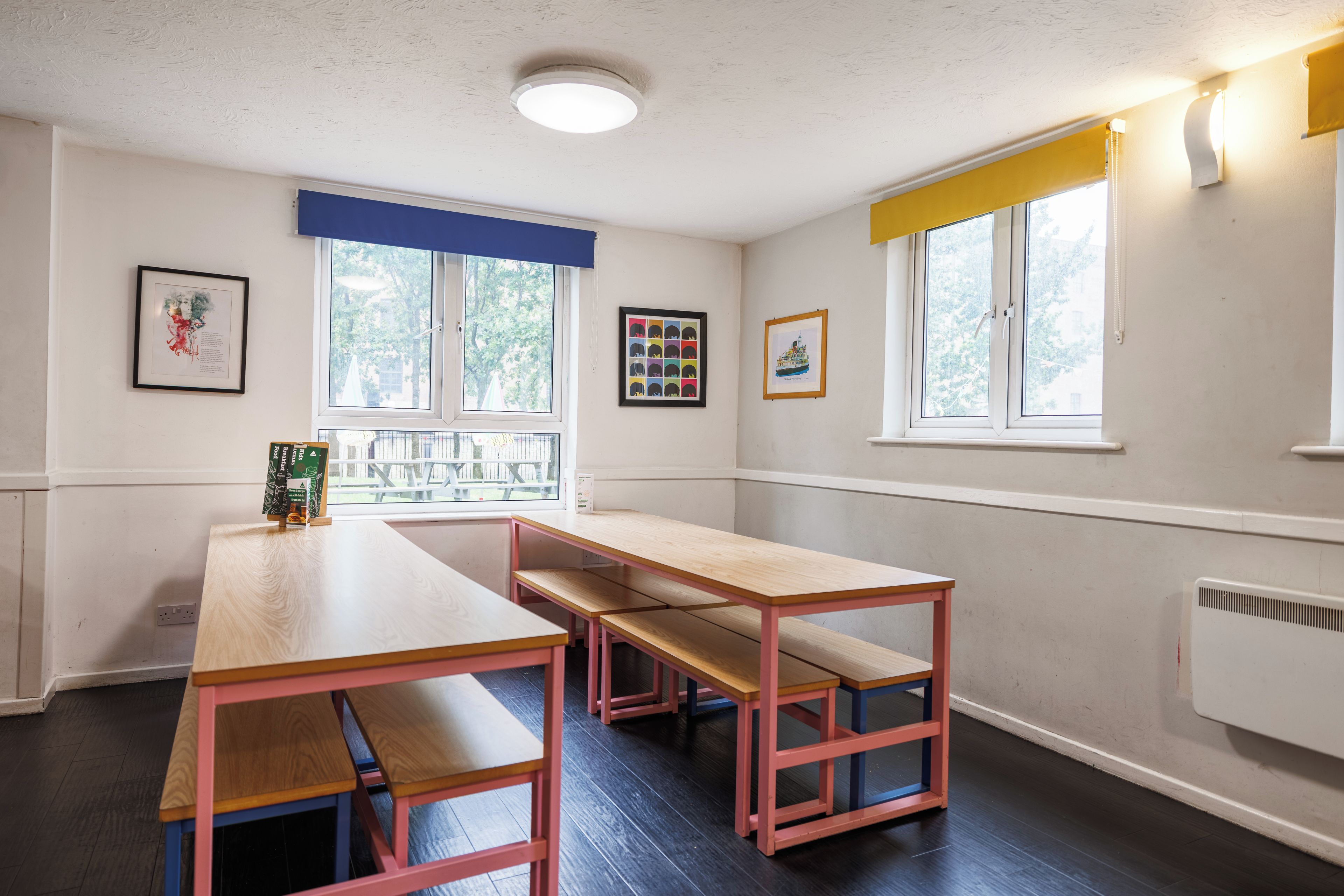 A room with a long table and benches, a window with a view, and framed artwork on the walls.