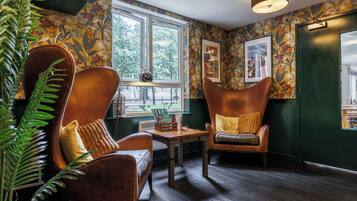 Een kamer met twee leren fauteuils, een houten tafel en een raam met uitzicht op bomen.