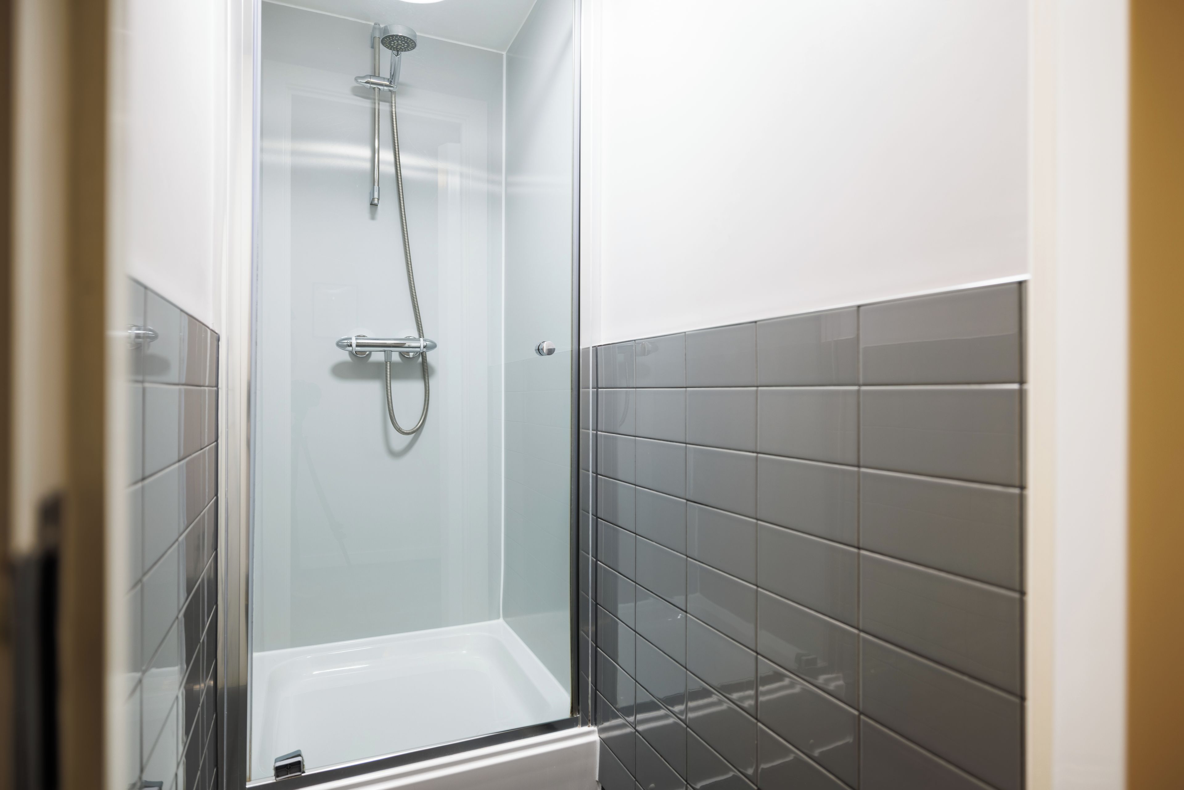 Une cabine de douche fermée par des parois en verre, dotée d’un pommeau de douche à main et d’un robinet mural.
