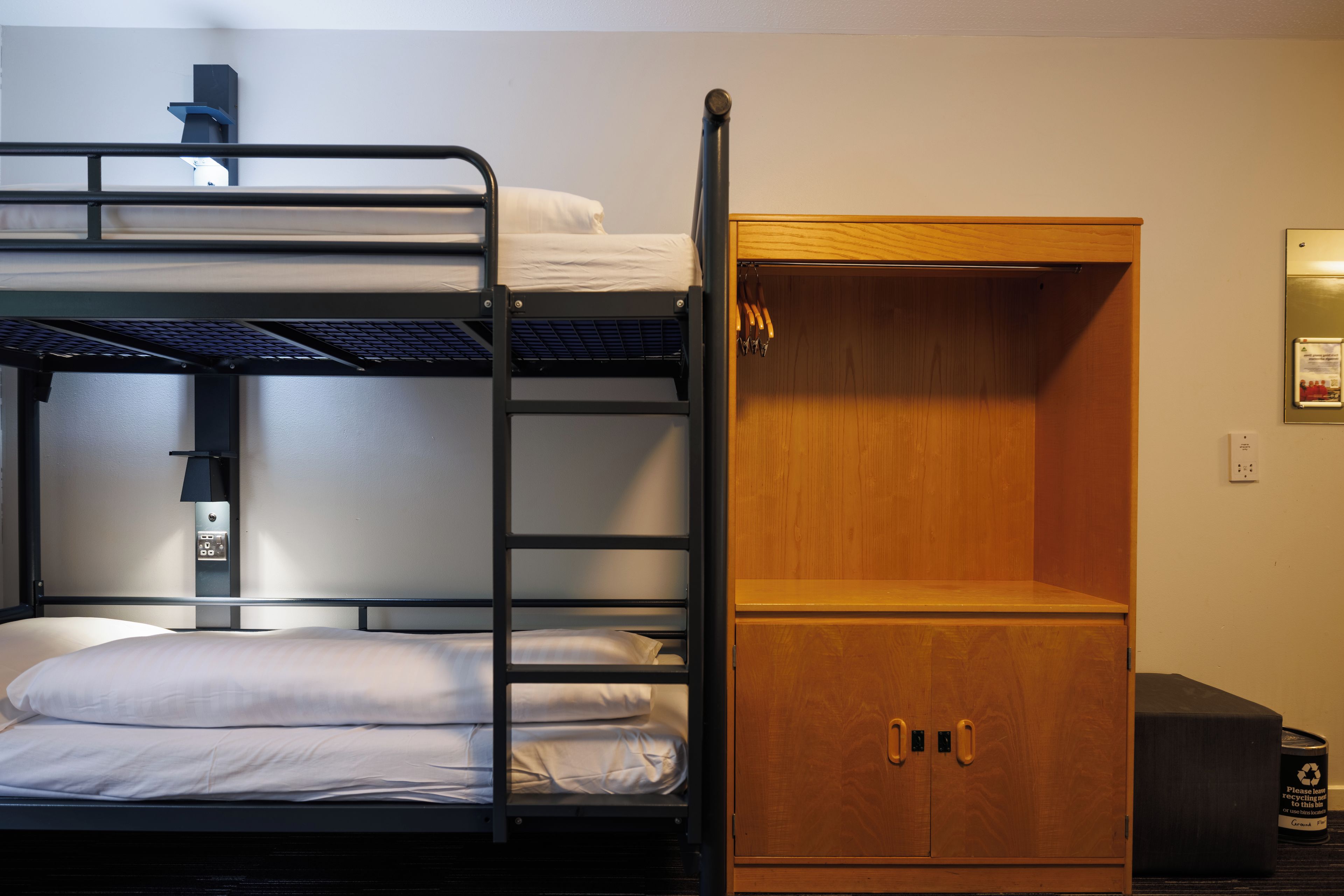 A bunk bed with a wooden wardrobe and a small trash bin.