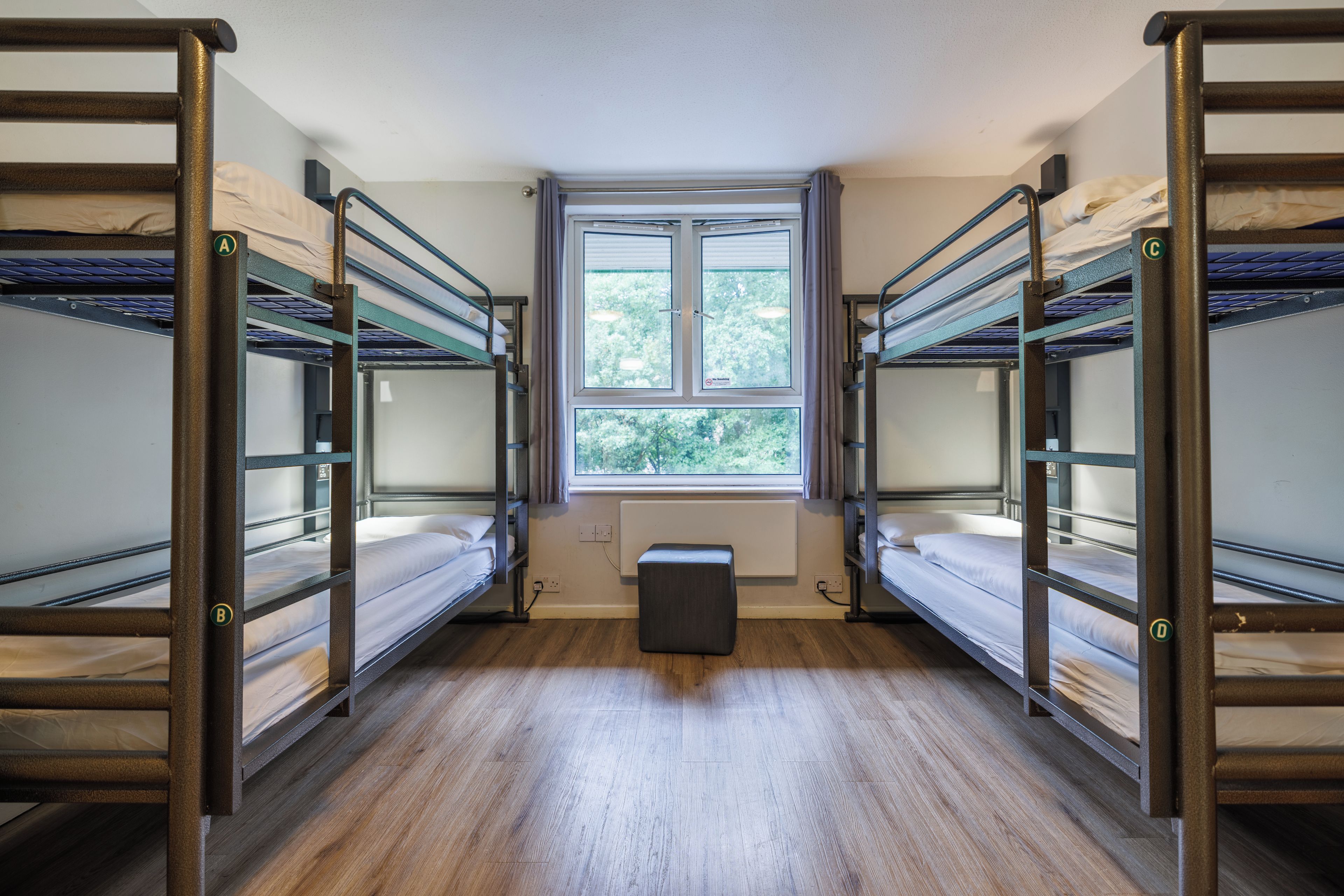 A dormitory room with bunk beds, a window, and a radiator.