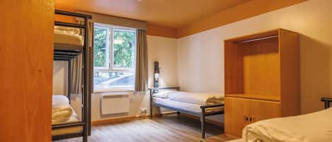 A compact room with bunk beds, a wooden wardrobe, a radiator, and a window with a view of greenery.