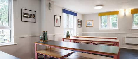 A classroom with wooden benches, white walls, and framed pictures.