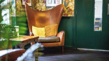 A room with a brown leather armchair with a yellow cushion, a wooden table, and a green wall with floral wallpaper.