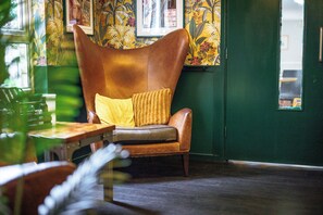 A room with a brown leather armchair with a yellow cushion, a wooden table, and a green wall with floral wallpaper. - YHA Liverpool Albert Dock - Hostel (Liverpool)