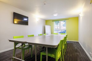 A conference room with a long table, green chairs, a whiteboard, and a television on the wall. - YHA Liverpool Albert Dock - Hostel (Liverpool)