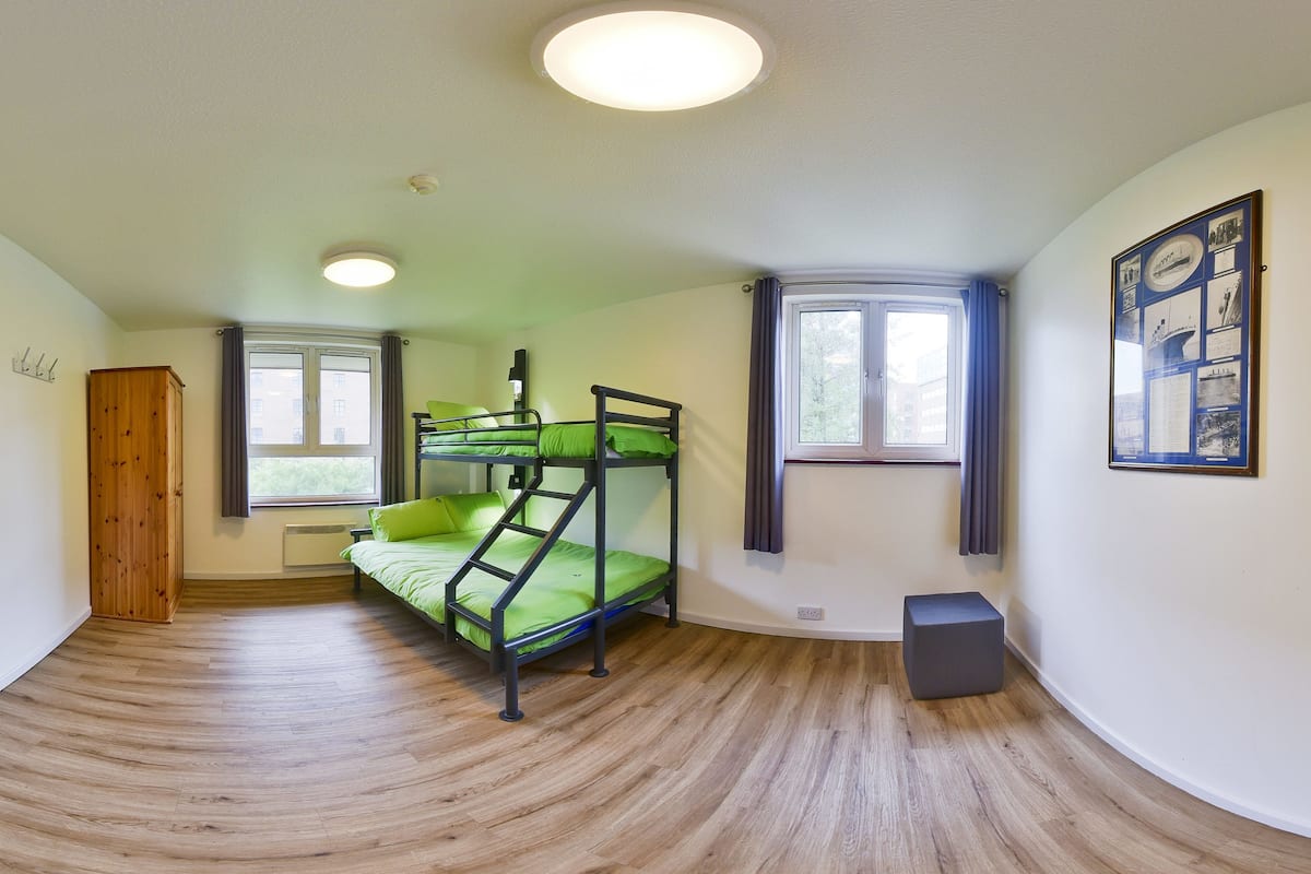 A room with bunk beds, a wooden wardrobe, a radiator, and a framed picture on the wall.