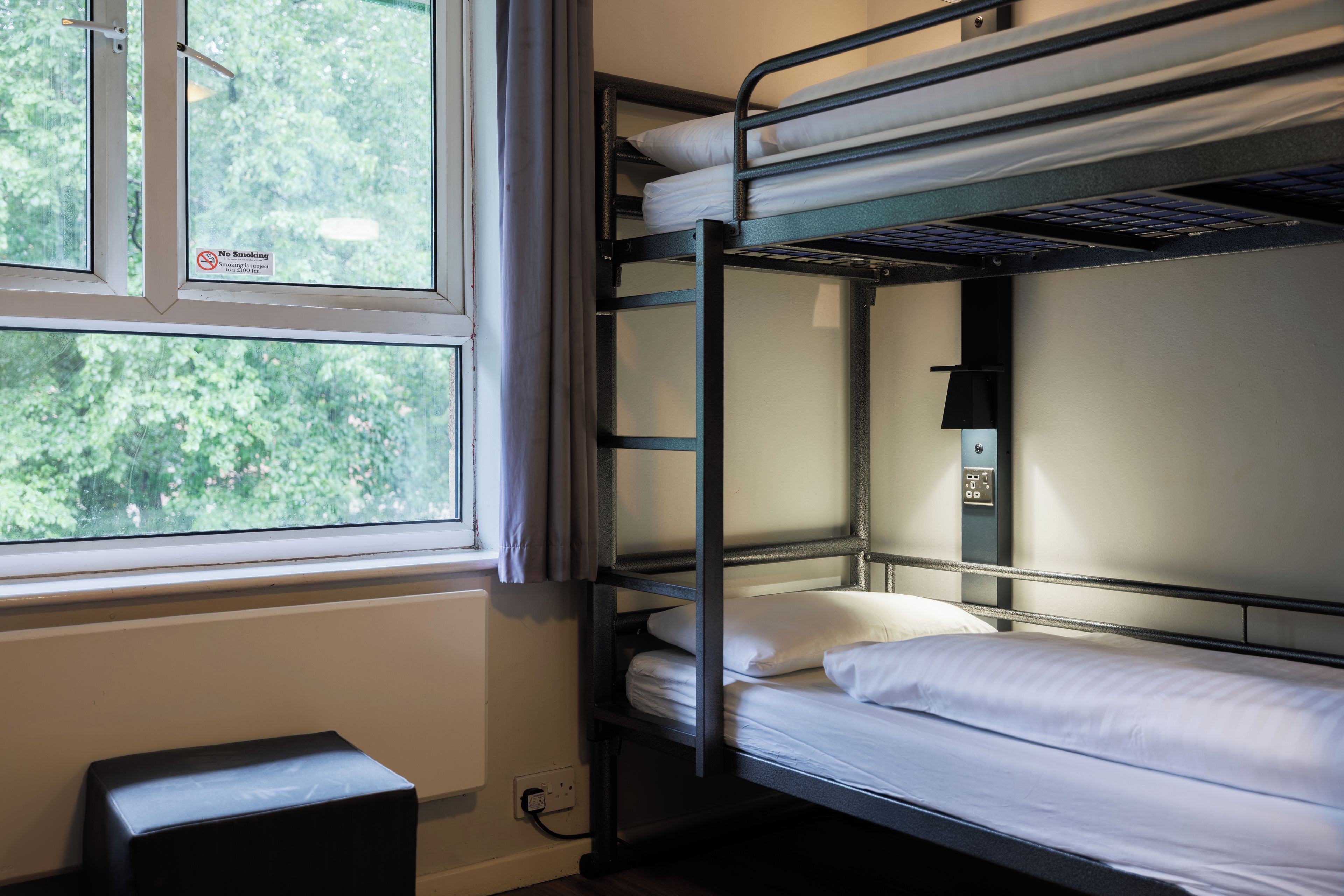 A bunk bed room with a window, a power outlet, and a 'No Smoking' sign.