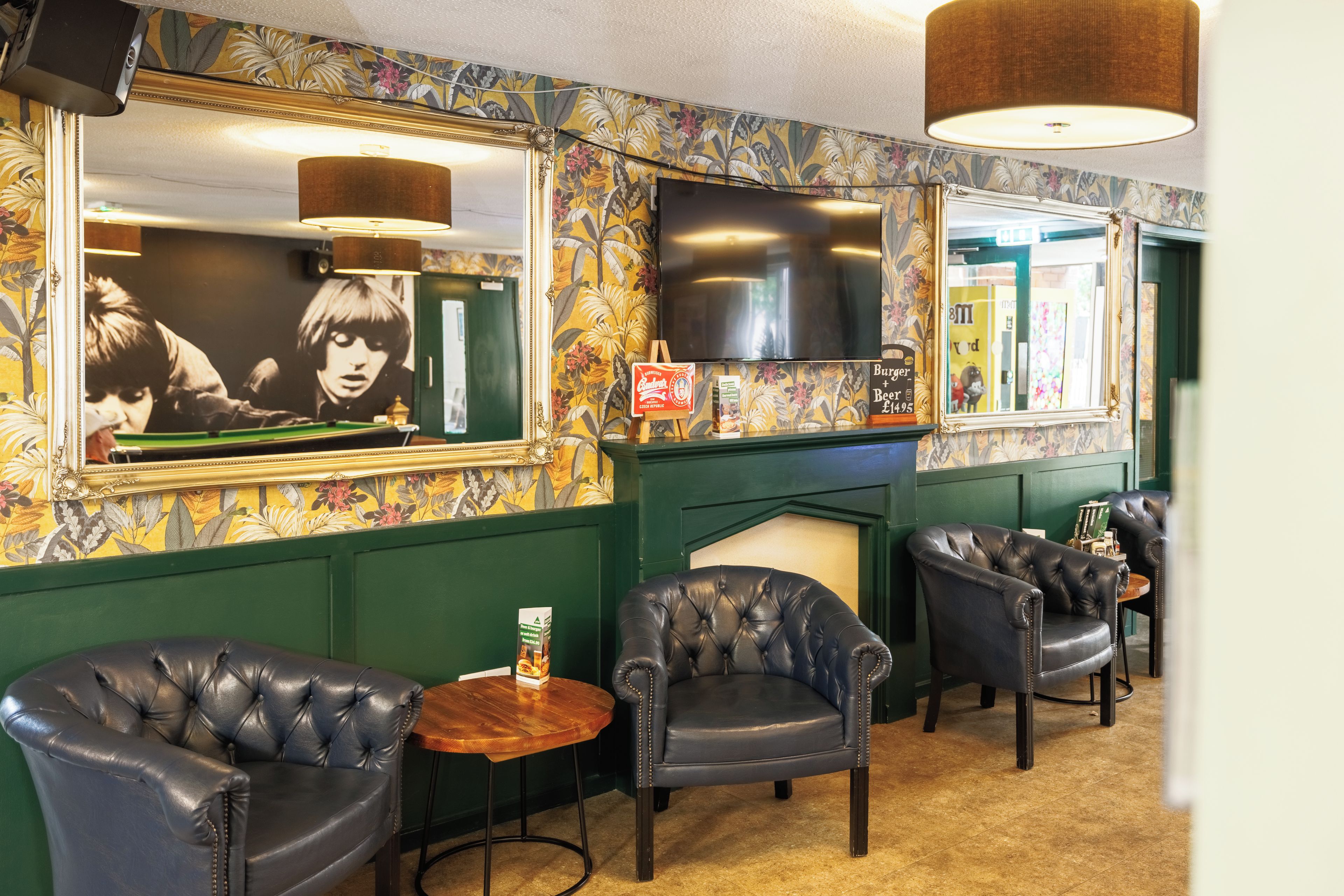 A room with a billiards table, two leather armchairs, a small round table, and a television mounted on the wall.