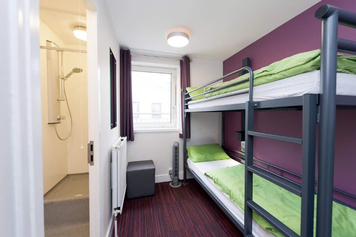 A compact room with bunk beds, a window, a shower, and a radiator.