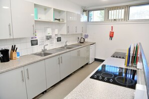 A modern kitchen with white cabinets, a stainless steel sink, a kettle, and a stove. - YHA London Thameside - Hostel (London)
