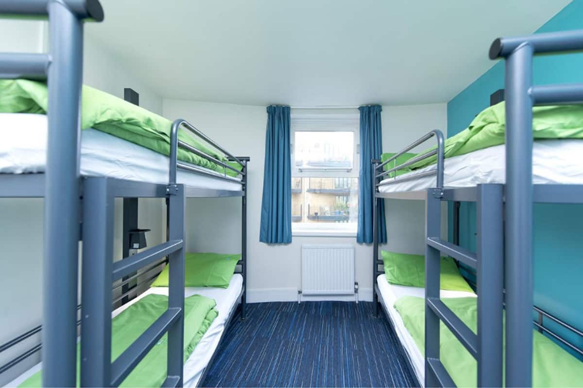 A dormitory room with bunk beds, a window with curtains, and a radiator.