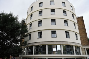 Un edificio de varios pisos con fachada curva, amplios ventanales en la planta baja y una chimenea de ladrillo.