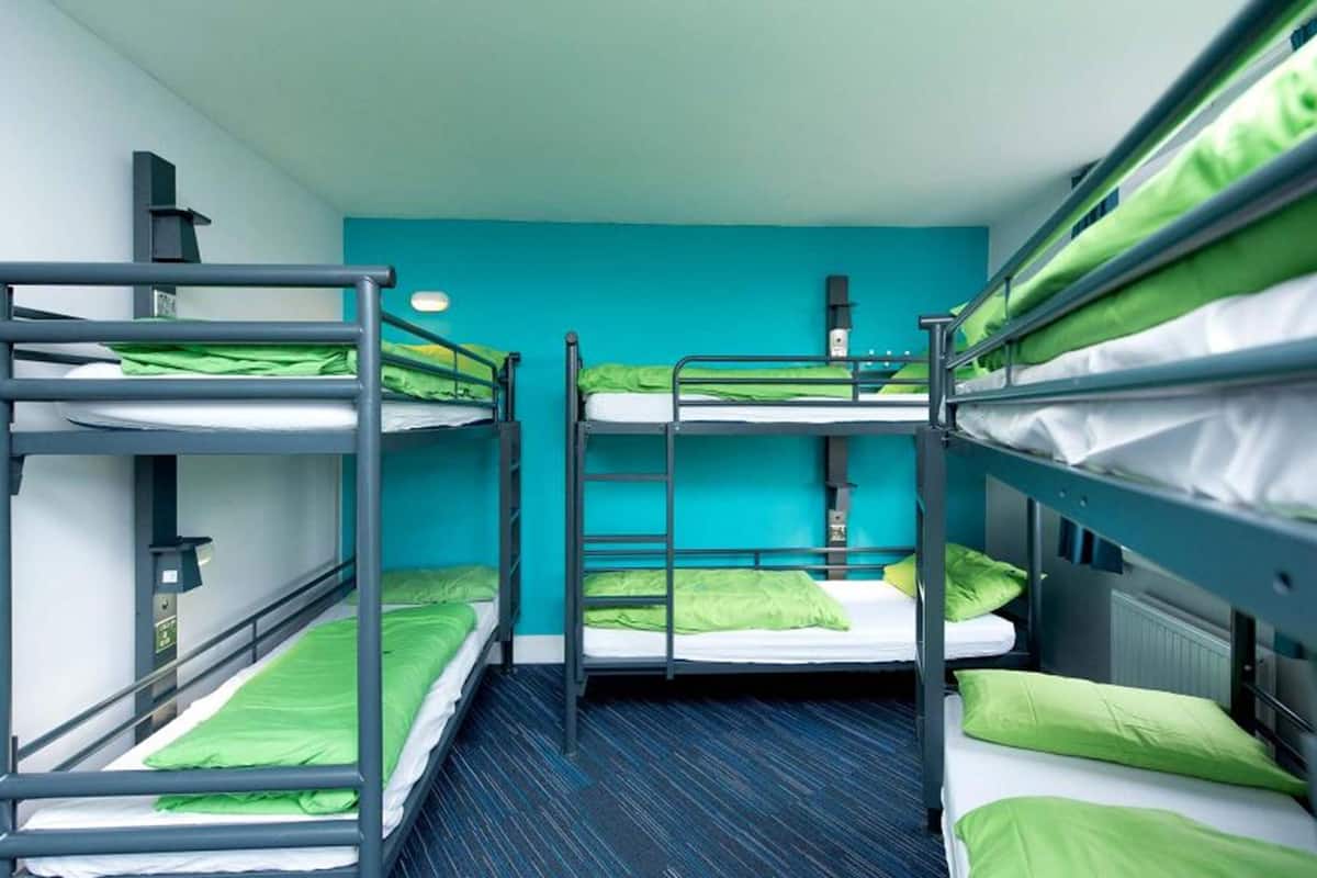 A dormitory room with bunk beds, teal walls, and a blue carpet.