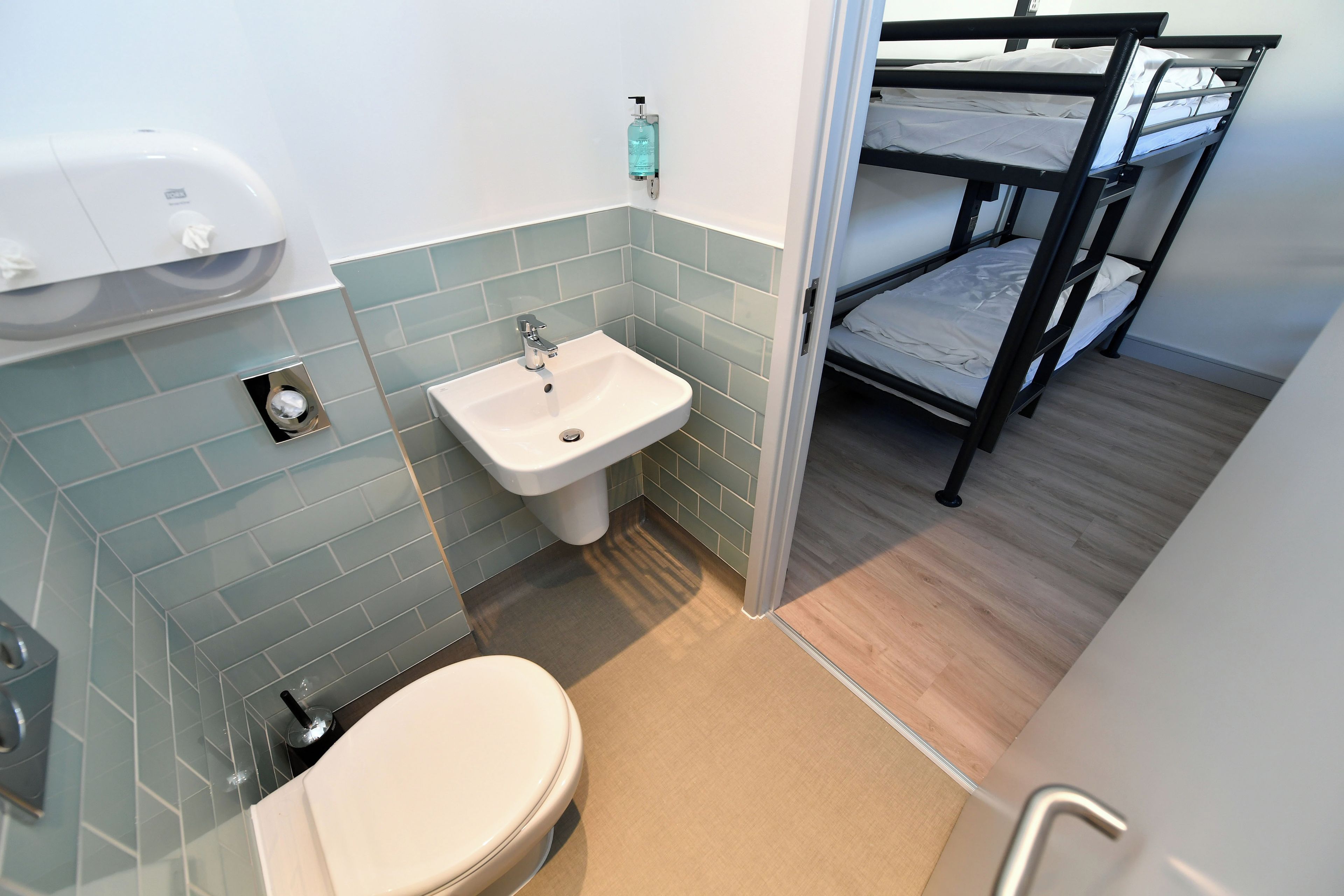 Un baño pequeño con lavamanos, inodoro y una cama individual en la habitación contigua.