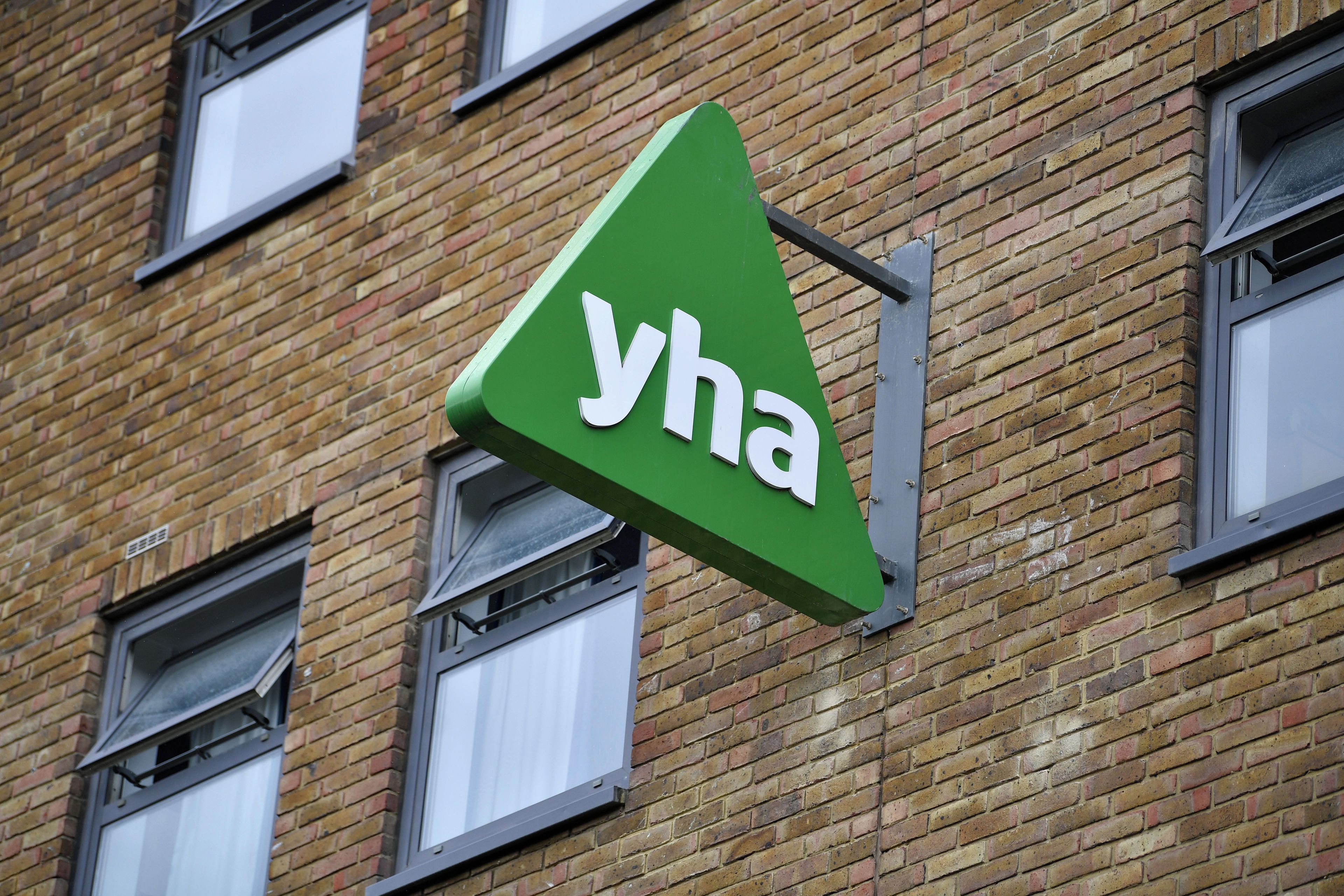 A green triangular sign with the letters 'yha' on a brick building.