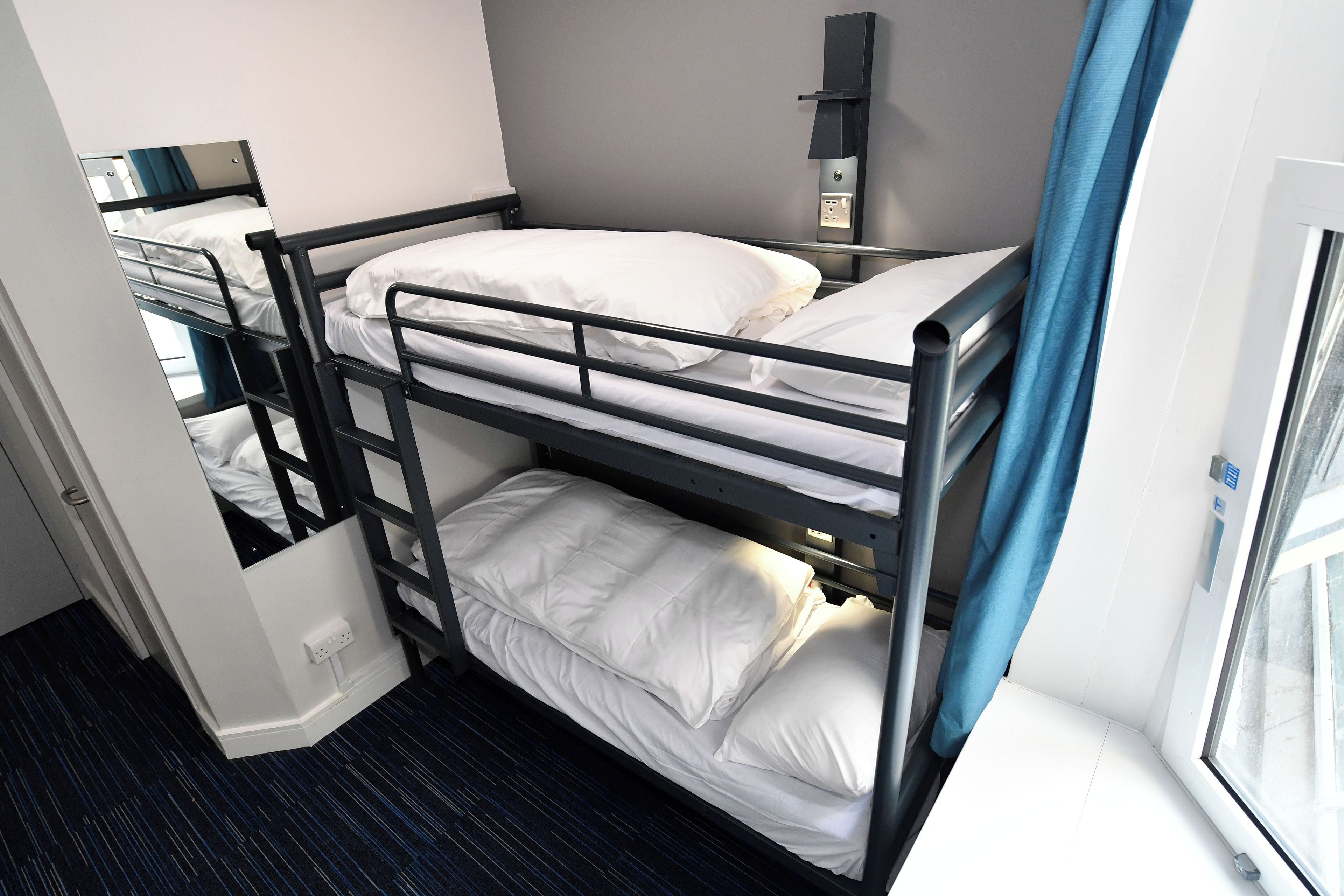 A bunk bed with a desk and a power outlet, a window with curtains, and a door.