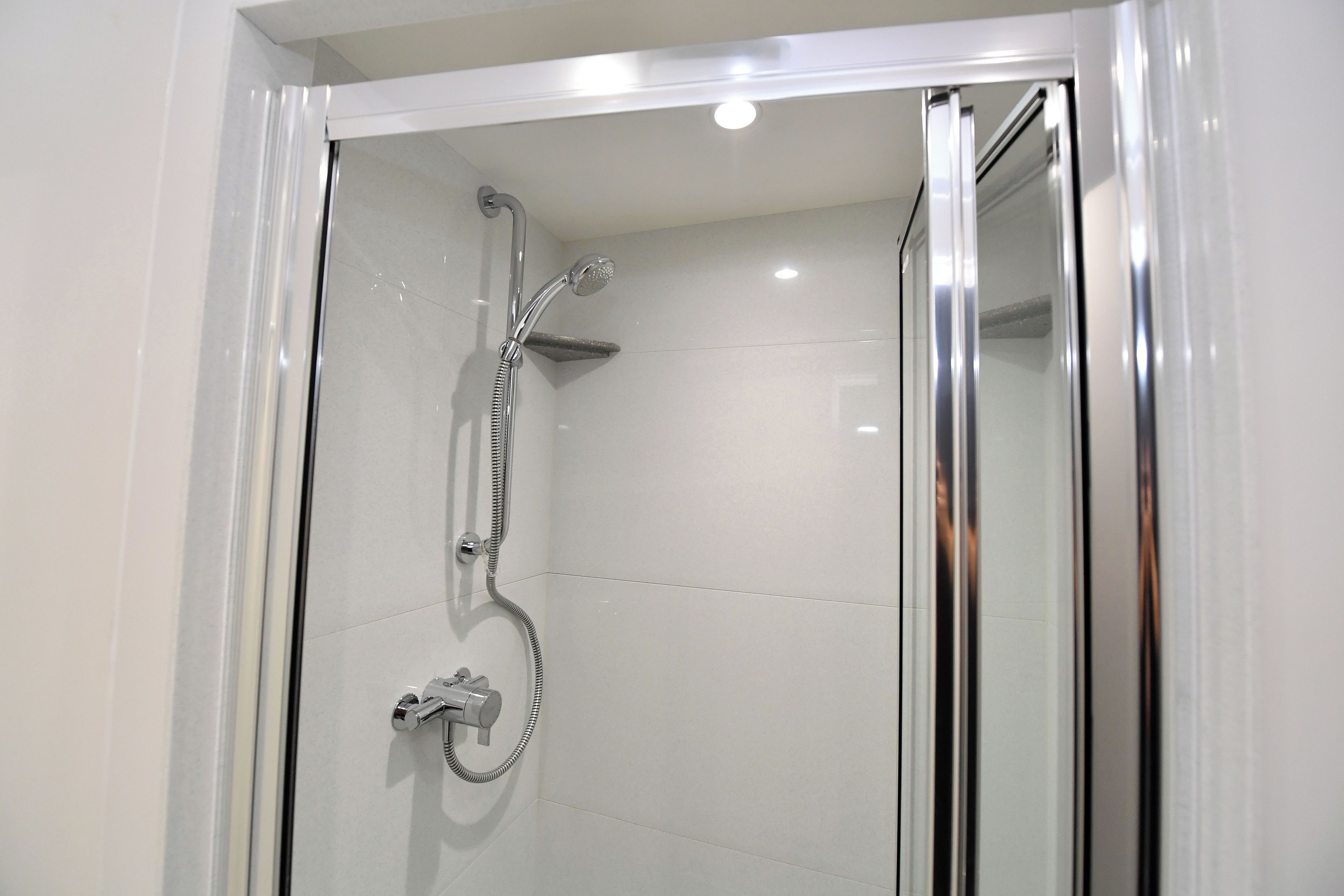 Une douche moderne avec une porte en verre, des accessoires chromés et un mur recouvert de carreaux.
