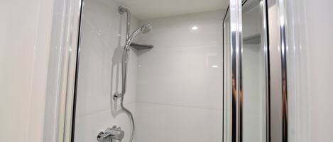 Une douche moderne avec une porte en verre, des accessoires chromés et un mur recouvert de carreaux.